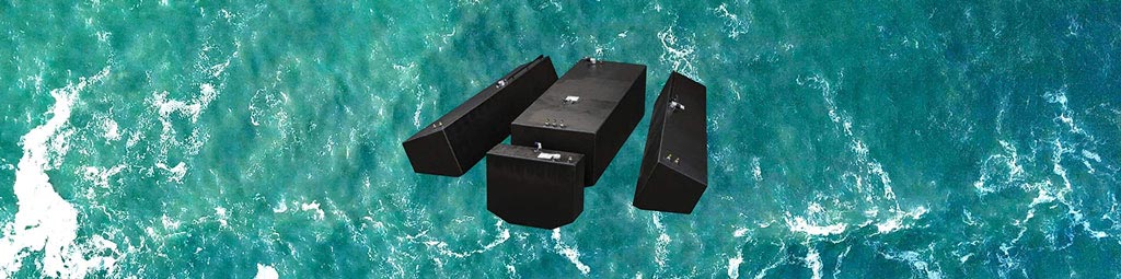 An aerial view of four black OEM replacement fuel tanks floating on the ocean, surrounded by turquoise water with white foam.