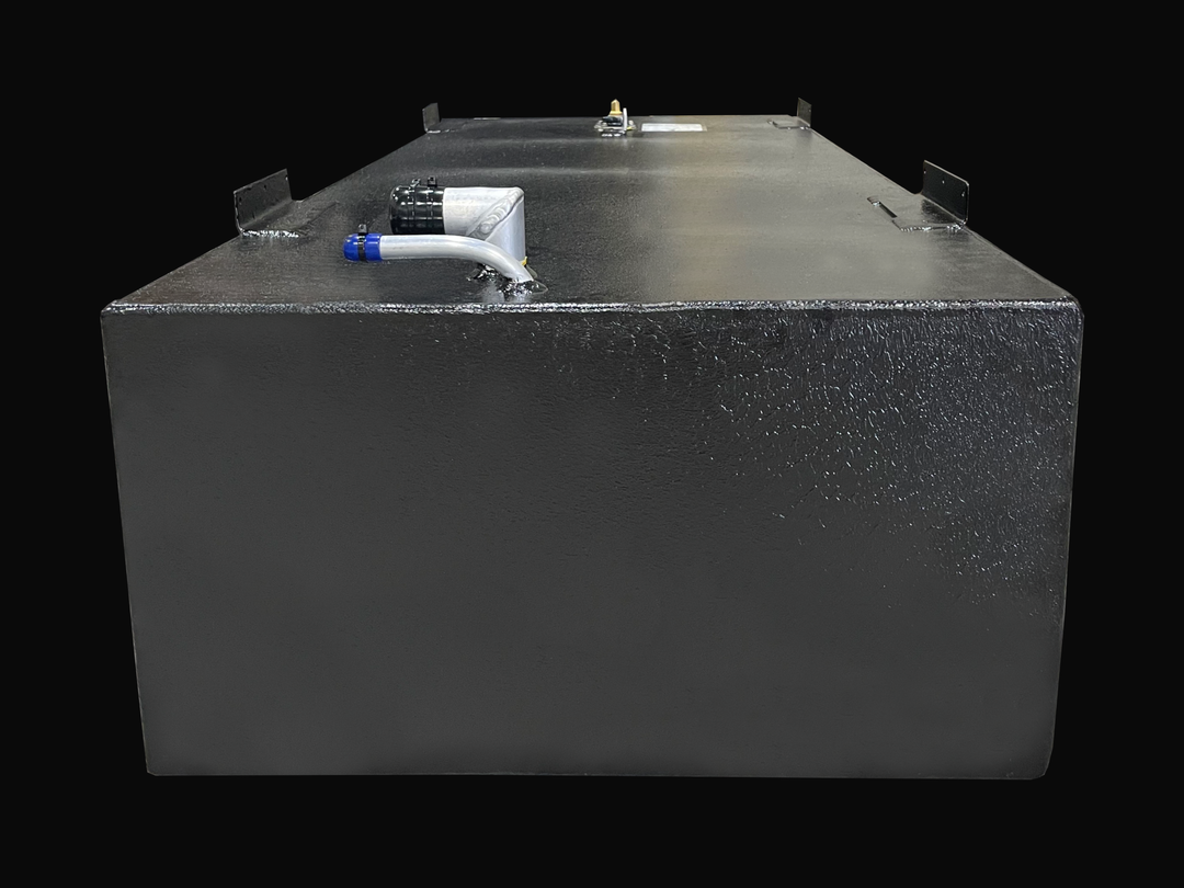 A wide, low-angle photo of a long, rectangular, dark, textured boat fuel tank. The top surface shows various fittings, including a white fitting with a blue hose connector near the front, and black mounting tabs on the corners, against a black background.