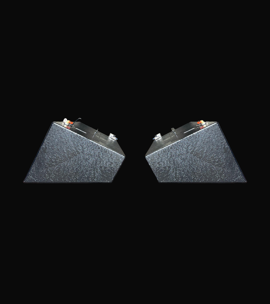 A profile photo showing the ends of a pair of dark, heavily-textured, wedge-shaped boat fuel tanks, isolated against a black background.