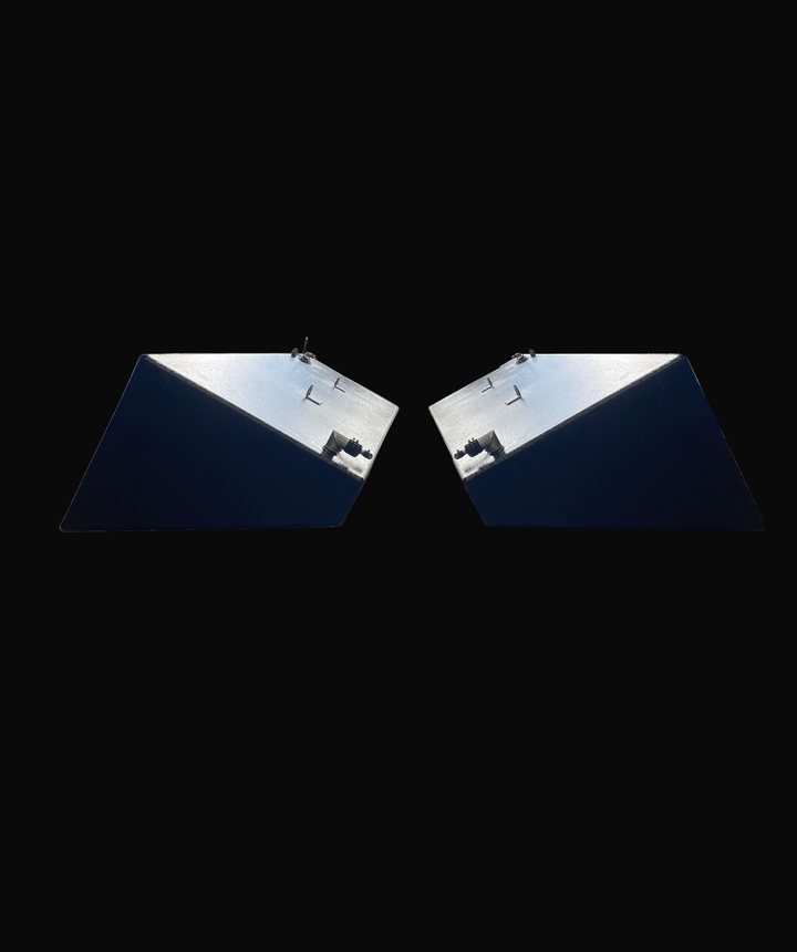 A low-angle view of a pair of dark, textured, wedge-shaped boat fuel tanks, showing their reflective angled bottoms and fittings, isolated against a black background.