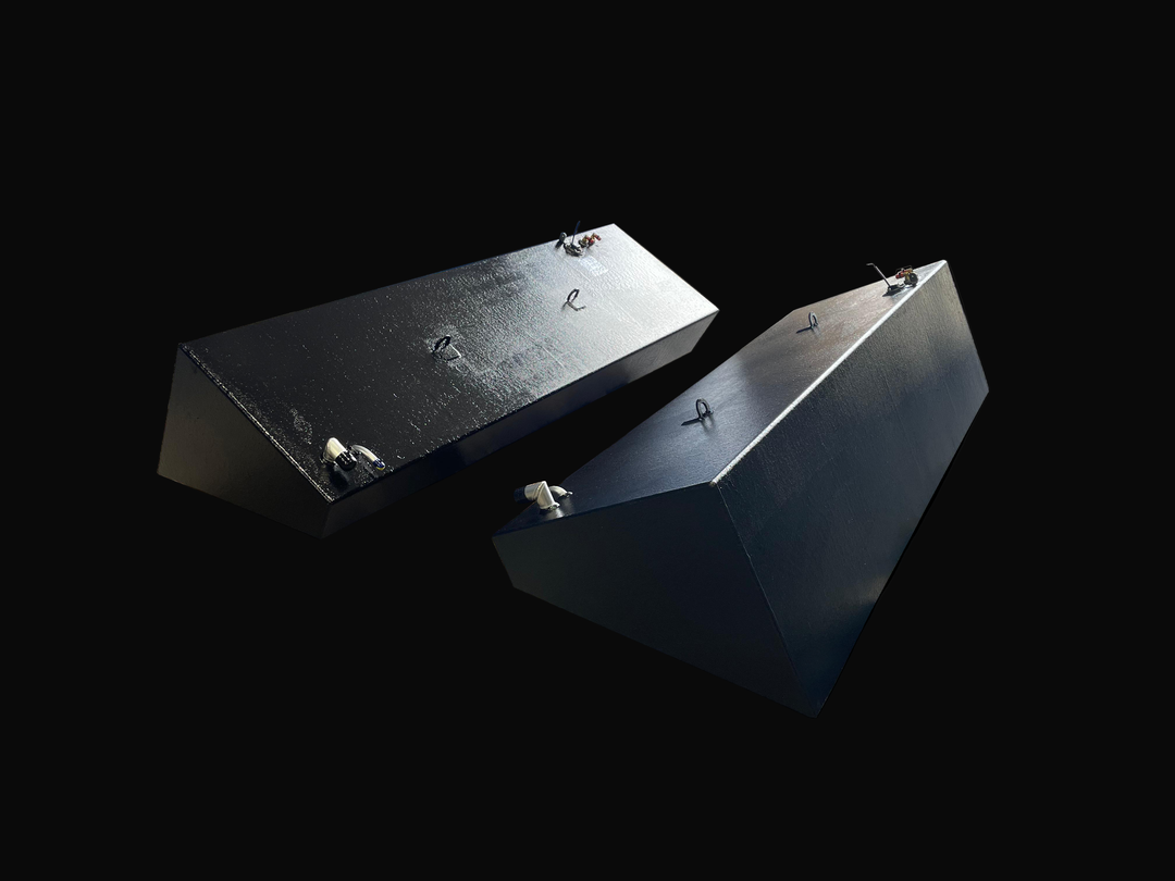 A photo of a pair of long, wedge-shaped boat fuel tanks with a dark, textured finish, shown side-by-side at an angle against a black background.
