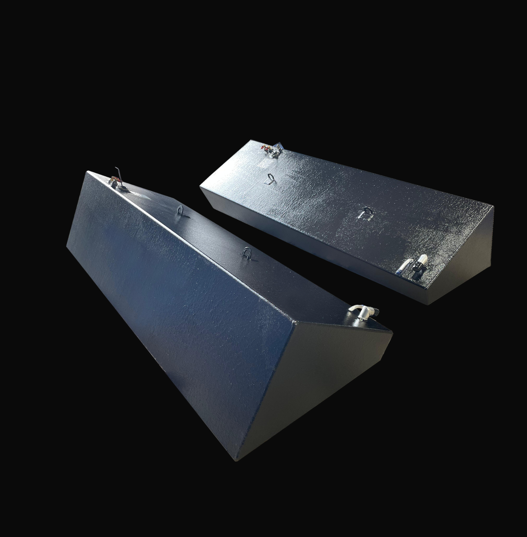 A photo of a pair of long, dark, textured, wedge-shaped boat fuel tanks, shown angled side-by-side from a high-angle perspective, against a black background.