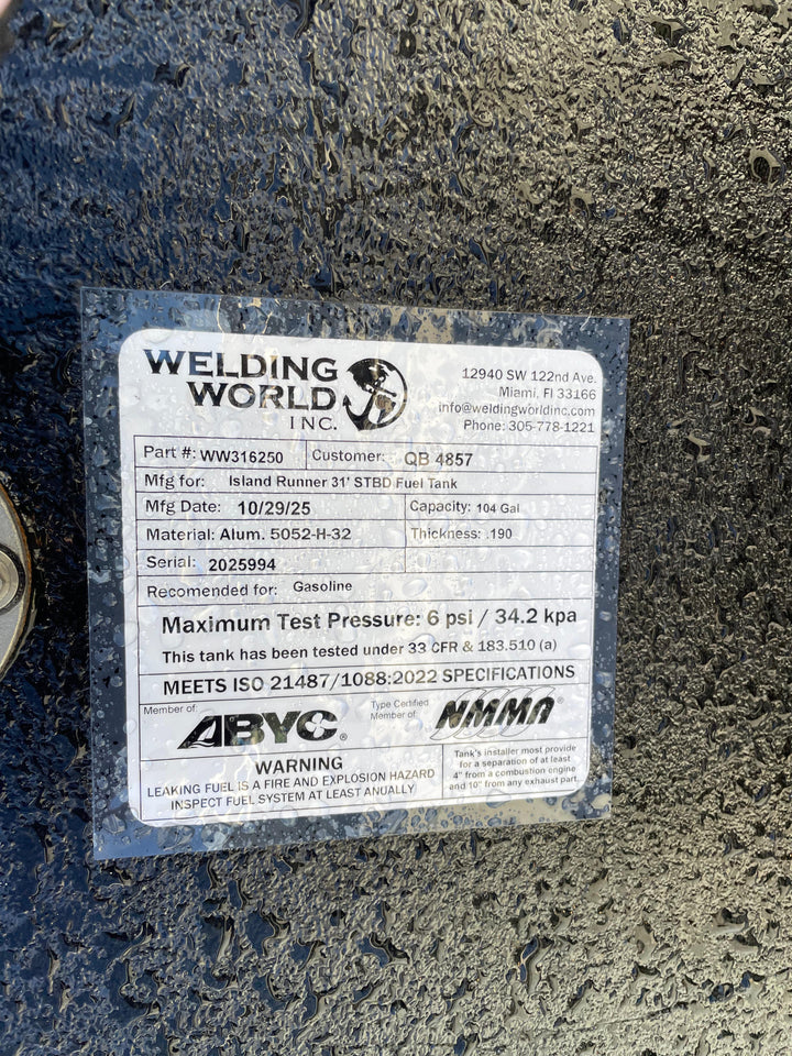 A close-up of a white specification label on a dark textured boat fuel tank. The Welding World Inc. label indicates it is for an "Island Runner 31' STBD Fuel Tank" with a 104-gallon capacity, part number WW316250.