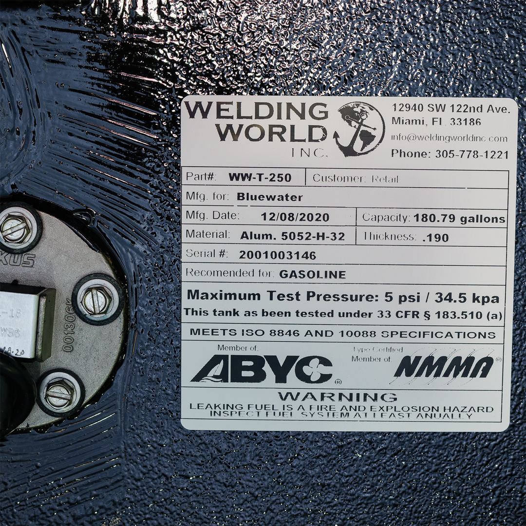 A close-up shot of a product label from "Welding World Inc." affixed to a textured black surface. The label details the product as "Part# WW-T-250," manufactured for Bluewater on December 8, 2020, with a capacity of 180.79 gallons. It specifies the material as "Alum. 5052-H-32" with a thickness of .190, serial # 2001003146, and recommended for gasoline. The label also states a maximum test pressure of 5 psi / 34.5 kpa and notes compliance with ISO 8846 and 10088 specifications, and is a member of ABYC/NMMA