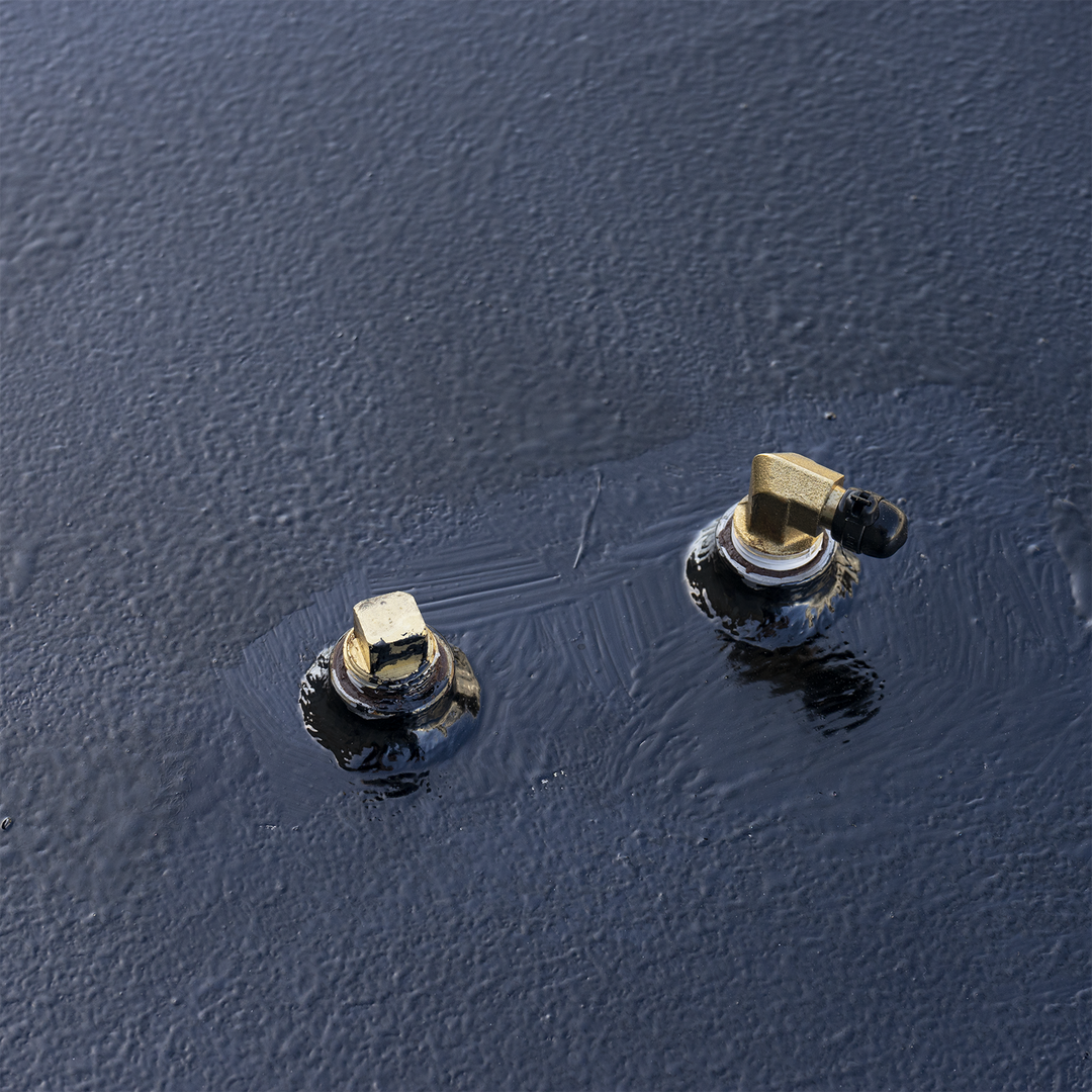 Detail view of the top-mounted components on a 117-gallon belly fuel tank for the 1995 Boston Whaler Outrage 21'. The image shows dual hex-head bolts embedded in a glossy black sealed surface, possibly indicating bonding or corrosion-resistant treatment. One bolt includes an attached brass or plated fitting, likely part of the fuel return or grounding path. The surrounding surface shows uneven application of the sealant, reinforcing its use in moisture resistance or dielectric isolation