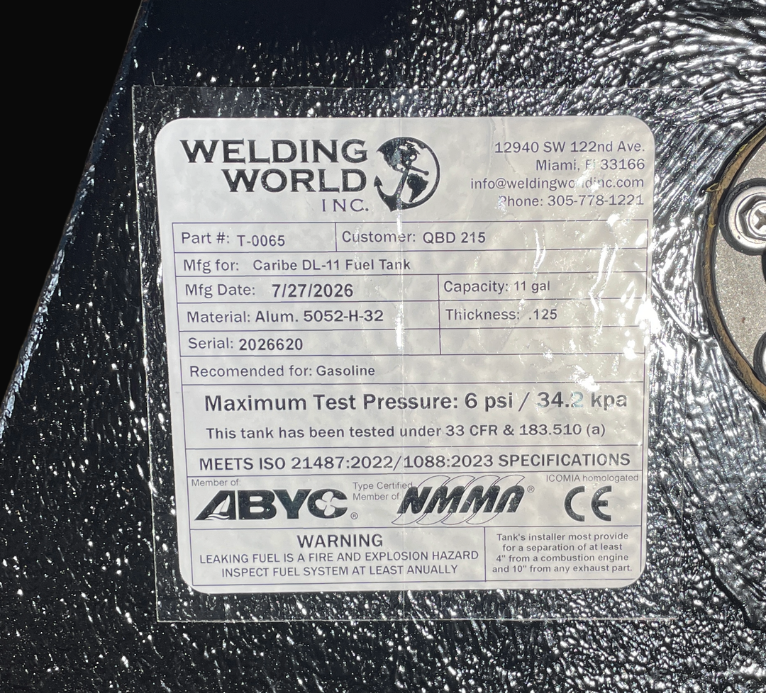 A macro top-down view of the official manufacturer certification tag on a physical, finished black encapsulated Caribe DL-11 OEM replacement marine fuel tank (11 gal 2016) from file image_aeb39a.jpg. Adhered to the textured black TarGard epoxy coating, the weather-resistant specification label from Welding World Inc. (Miami, FL) lists part number T-0065, heavy-gauge Alum. 5052-H-32 material, .125 thickness, an 11 gal capacity, gasoline recommendation, 6 psi / 34.2 kpa maximum test pressure under 33 CFR & 18