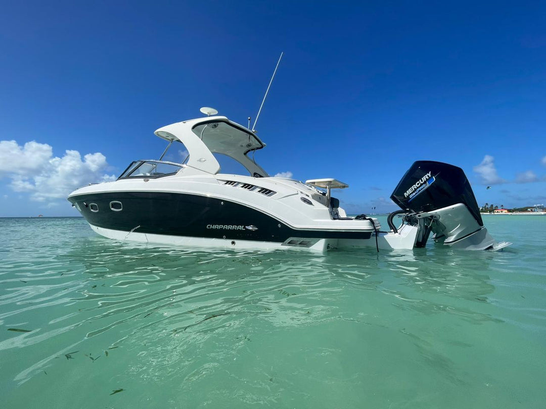 A white Chaparral 327 SSX boat floating in clear turquoise water under a blue sky, with a black Mercury outboard engine at the stern. The image captures the boat from a side angle, showing its sleek design and the engine partially submerged
