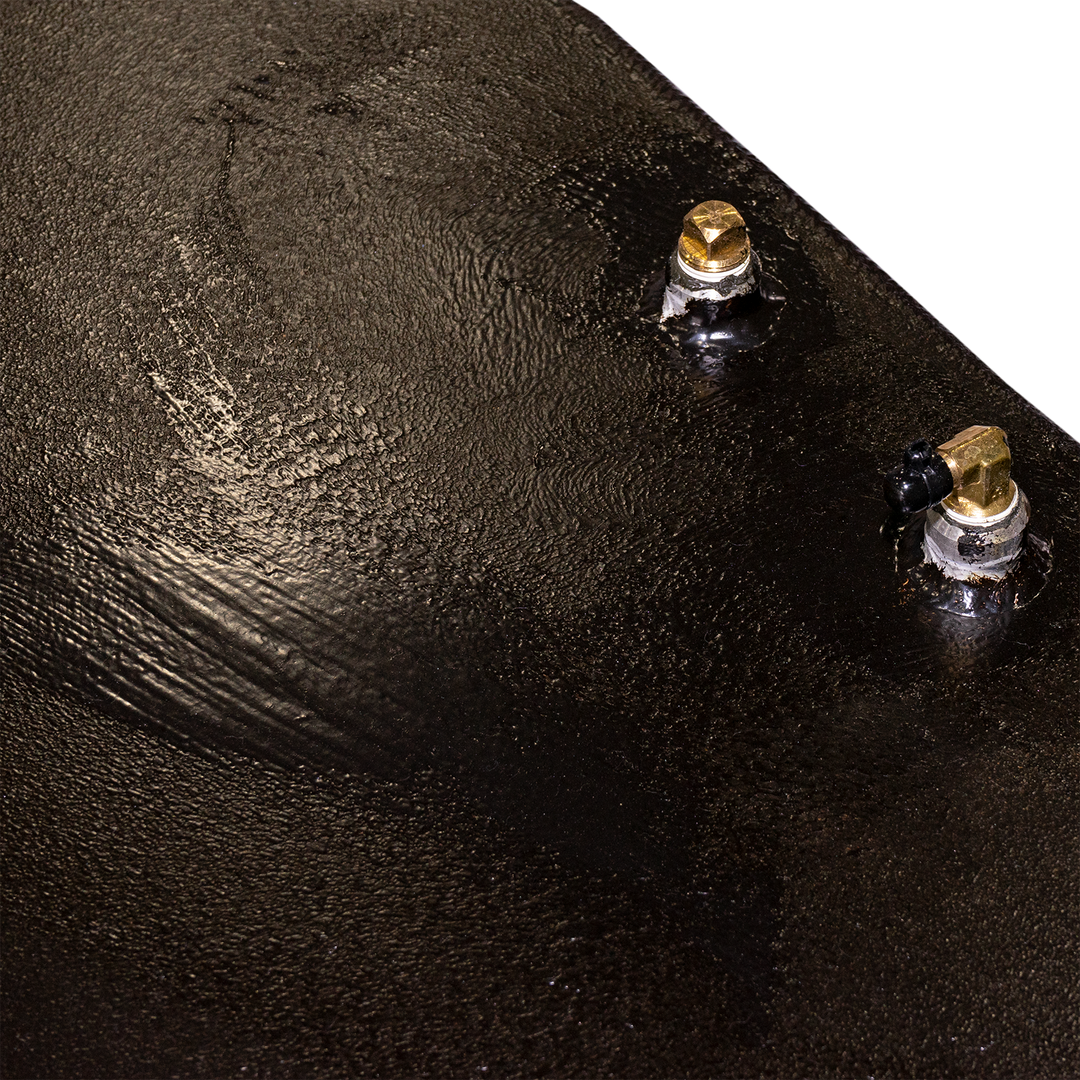  A close-up of a black, textured surface, likely part of a fuel tank, with two brass-colored fittings protruding from it. One fitting is a straight connector, and the other is an angled connector with a black tip. The background is a checkerboard pattern