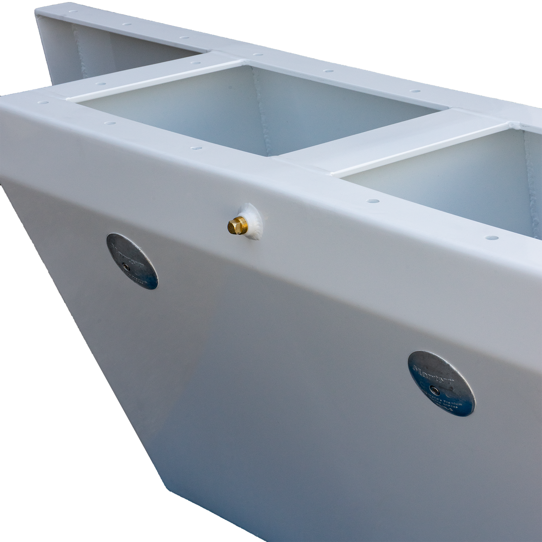 A close-up view of a custom-built Apex Mk. II twin engine bracket, featuring a white, rectangular structure with two circular blue labels on the sides and a small brass fitting on the front. The bracket has an open top with a rectangular cutout in the center. The background is transparent