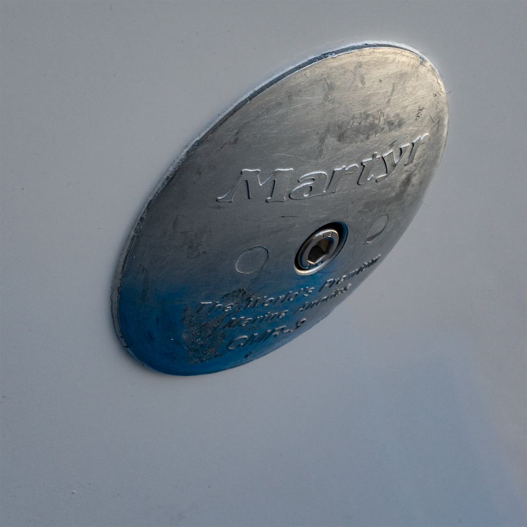 Close-up of a metallic circular plate labeled "Martyr," featuring a central hole and engraved text, mounted on a white surface