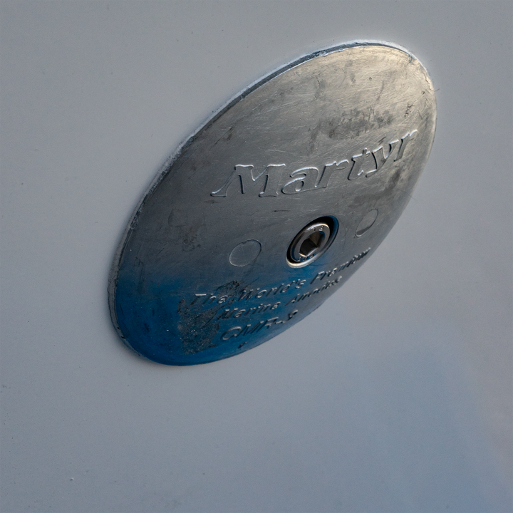 Close-up of a metallic circular plate labeled "Martyr," featuring a central hole and engraved text, mounted on a white surface