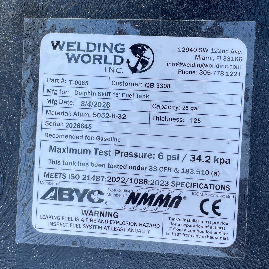 A close-up extreme macro photo displaying the official compliance specification decal label attached to the black epoxy deck of a physical Dolphin Skiffs 16 OEM replacement marine fuel tank (25 gal 1998) from file image_432d73.jpg. Printed by manufacturer Welding World Inc. in Miami, FL, the specification tag details key manufacturing data: Part # T-0065, Customer QB 9308, Mfg Date 8/4/2026, Capacity 25 gal, Material Alum. 5052-H-32, Thickness .125, Serial 2026645, and Recommended for Gasoline. Safety ratin