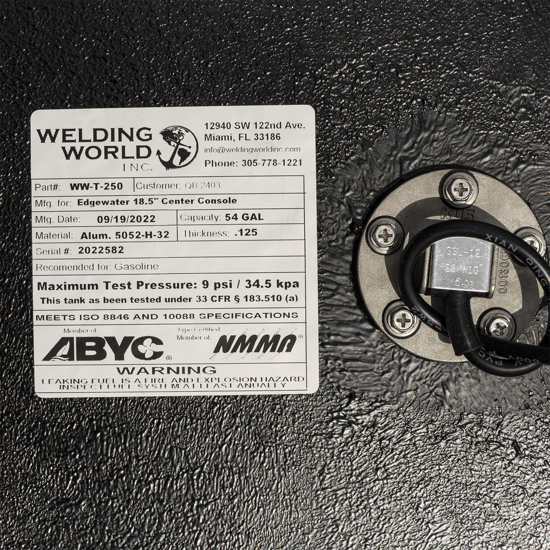 A close-up view of a manufacturer's label and a round fuel sending unit on a heavily textured black surface. On the left, the white "Welding World, Inc." label specifies the tank is for an "Edgewater 18.5" Center Console" with a 54-gallon capacity, made on September 19, 2022. On the right, the silver fuel sending unit is secured with four screws, with a black wire emerging from its center. The label also features ABYC and NMMA compliance logos