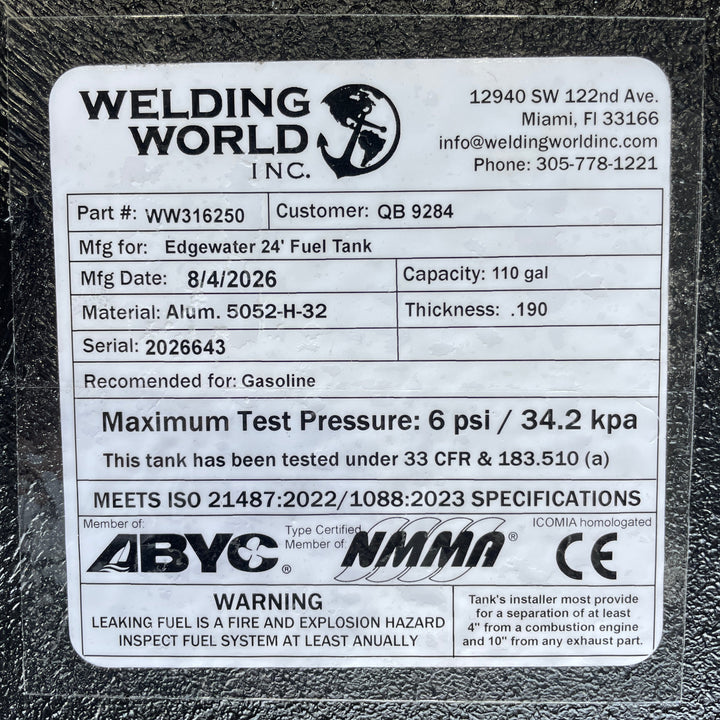 A studio macro close-up view displaying the official manufacturer certification data label on an Edgewater 24 OEM replacement marine fuel tank (110 gal) from file image_f68475.jpg, encapsulated under protective clear laminate on a black TarGard epoxy coated surface. Printed specifications verify fabrication details by Welding World Inc. in Miami, FL, including Part Number WW316250, Serial 2026643, 110-gallon capacity, .190" thickness 5052-H32 aluminum construction, 6 psi / 34.2 kPa maximum test pressure rat
