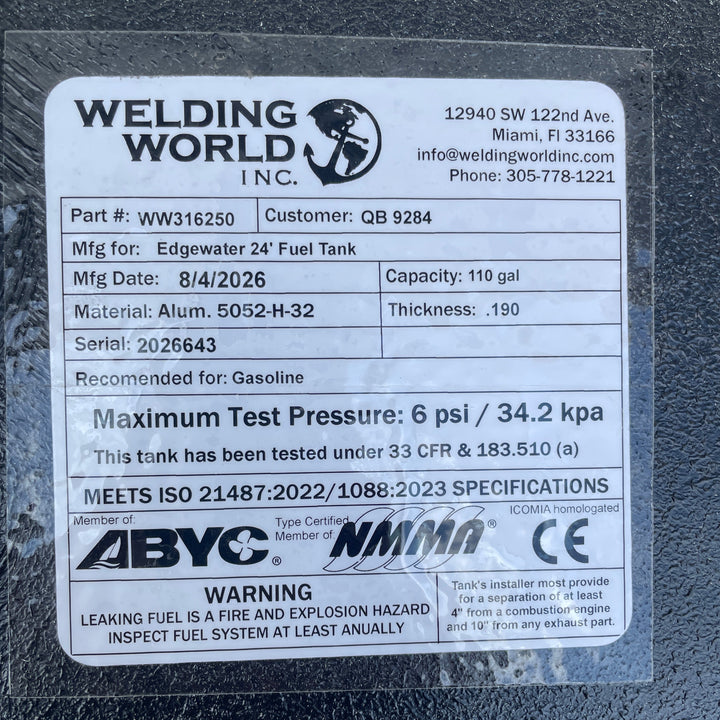 A studio macro close-up view displaying the official manufacturer certification data label on an Edgewater 24 OEM replacement marine fuel tank (110 gal) from file image_f62da8.jpg, encapsulated under protective clear laminate on a black TarGard epoxy coated surface. Printed specifications verify fabrication details by Welding World Inc. in Miami, FL, including Part Number WW316250, Serial 2026643, 110-gallon capacity, .190" thickness 5052-H32 aluminum construction, 6 psi / 34.2 kPa maximum test pressure rat
