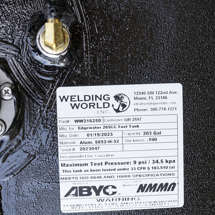 Label on a black textured surface showing Welding World Inc. contact info and tank specifications. Part number WW316250, made for Edgewater 265CC Fuel Tank, manufactured 01/19/2023, capacity 203 gallons, aluminum material, thickness .190, serial number 2023047. Rated for gasoline with maximum test pressure 9 psi / 34.5 kPa. Meets ISO 8846 and 10088 specifications. Member of ABYC and NMMA. Warning about fire and explosion hazard from leaking fuels