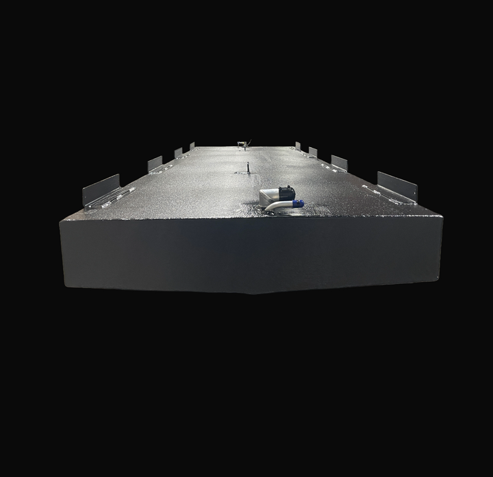 A studio low-angle front end view highlighting the subtle V-bottom deadrise contour and symmetrical mounting profile of a physical, finished black encapsulated Fountain 24 OEM replacement marine fuel tank (130 gal) from file image_c45fe6.jpg, isolated against a black background. Precision-fabricated from heavy-gauge .190" marine-grade 5052-H32 aluminum, the elongated hull-conformed cell is fully encapsulated in a protective, textured black TarGard epoxy coating to resist severe saltwater pitting and bilge m