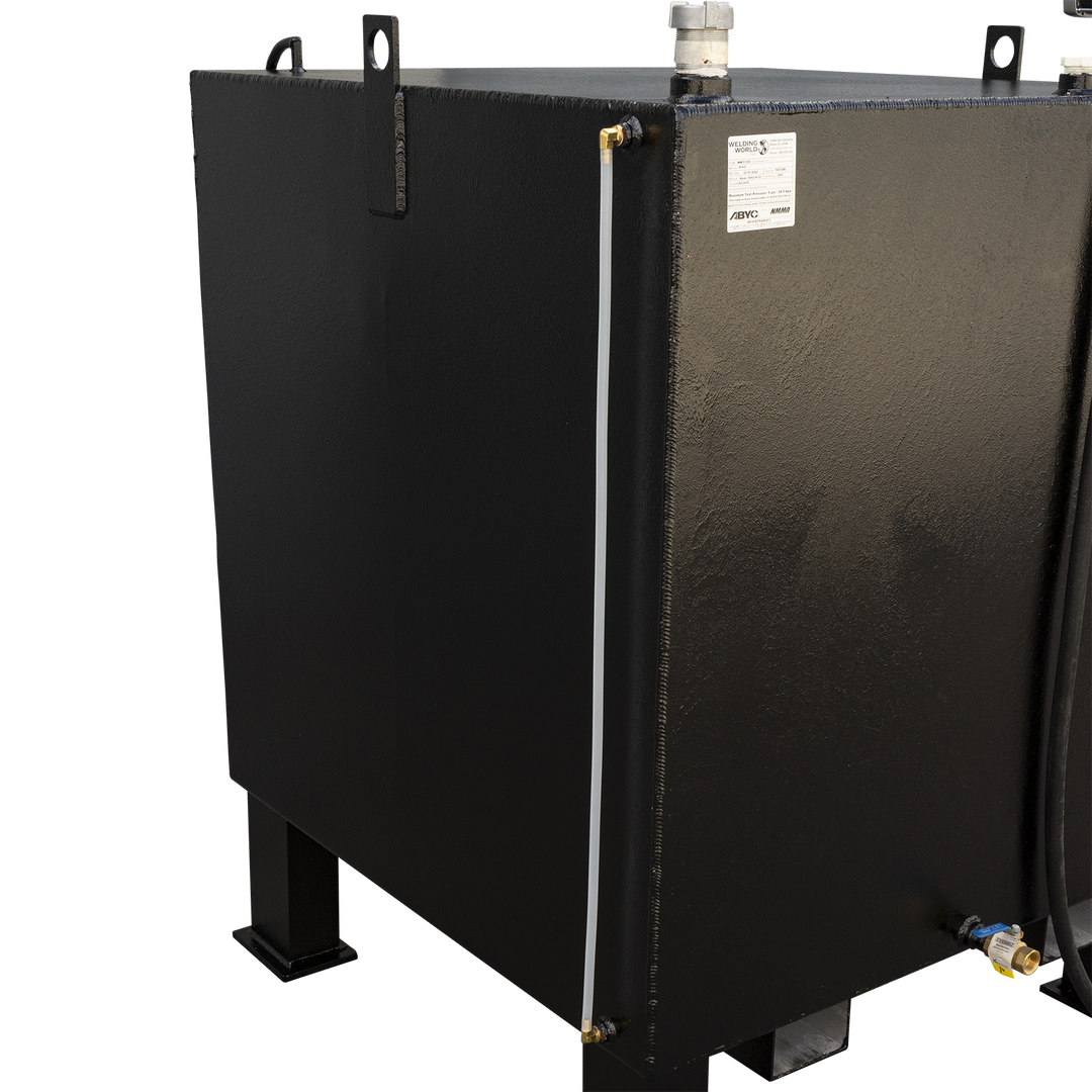 A black, rectangular fuel tank with a textured finish, viewed from a slight angle. It has four sturdy legs, one visible in the front left. A white translucent tube runs vertically along the left side, and a white cap is on the top surface. A black hose is visible on the right side of the tank, and a brass valve with a blue handle is near the bottom right. A white label is affixed to the front of the tank