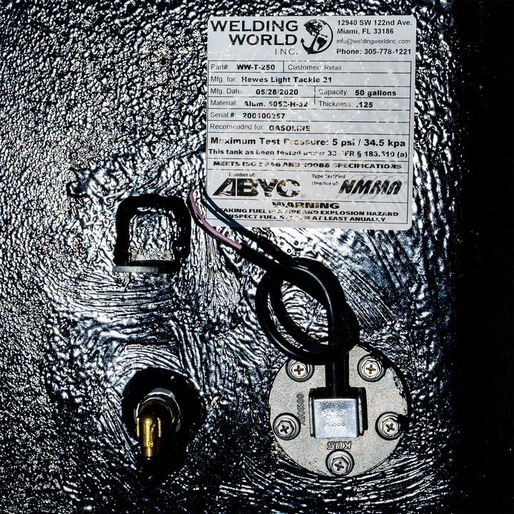 Close-up of a 1994 Hewes Light Tackle 21' belly fuel tank with a 56-gallon capacity. The tank features a label from Welding World, Inc., detailing customer information and specifications, including a maximum test pressure of 5 psi. The tank is equipped with a fuel gauge and a fuel line connection