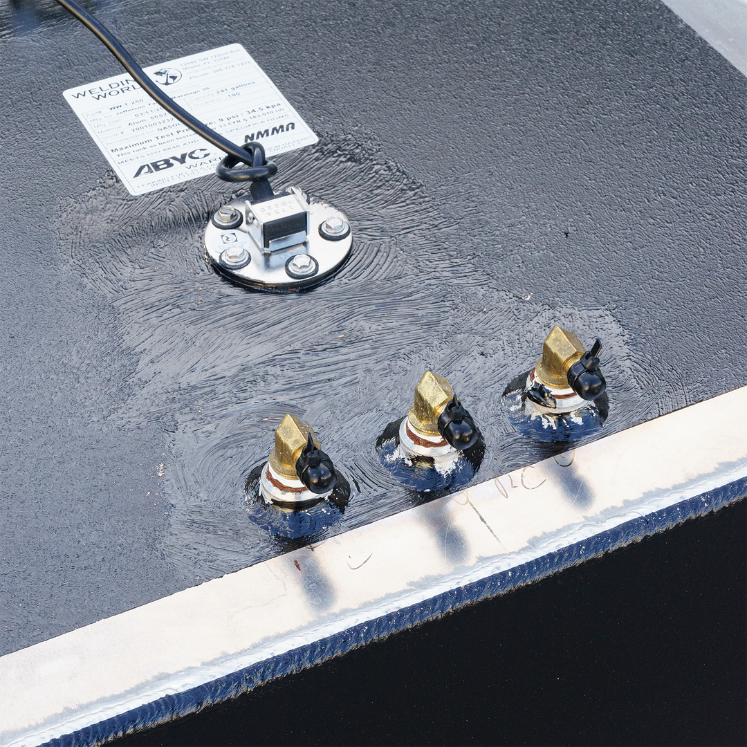 A close-up of a black, textured fuel tank surface with a lighter gray border. Three brass-colored fittings with black caps are visible, along with a circular metal plate secured by screws, from which a black wire extends. A white product label from "Welding World Inc." providing specifications for a Jefferson Yachts Maralago 35' 1997 - 241 gal. OEM Replacement Fuel Tank is attached to the tank surface