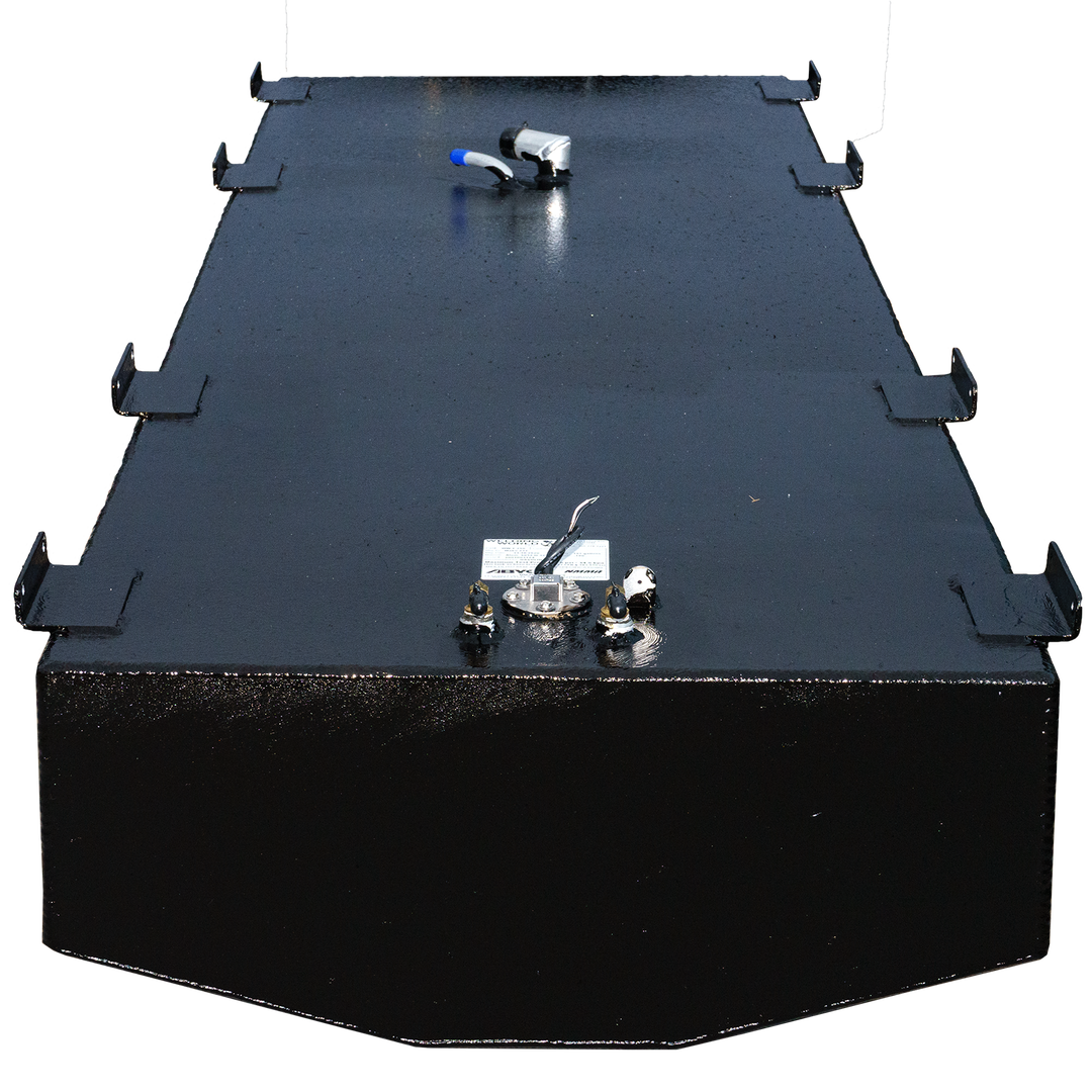 A top view of a rectangular black fuel tank, featuring a smooth surface with multiple ports, including a fuel gauge and connectors. The tank is equipped with metallic fittings and a warning label, set against a transparent checkered background