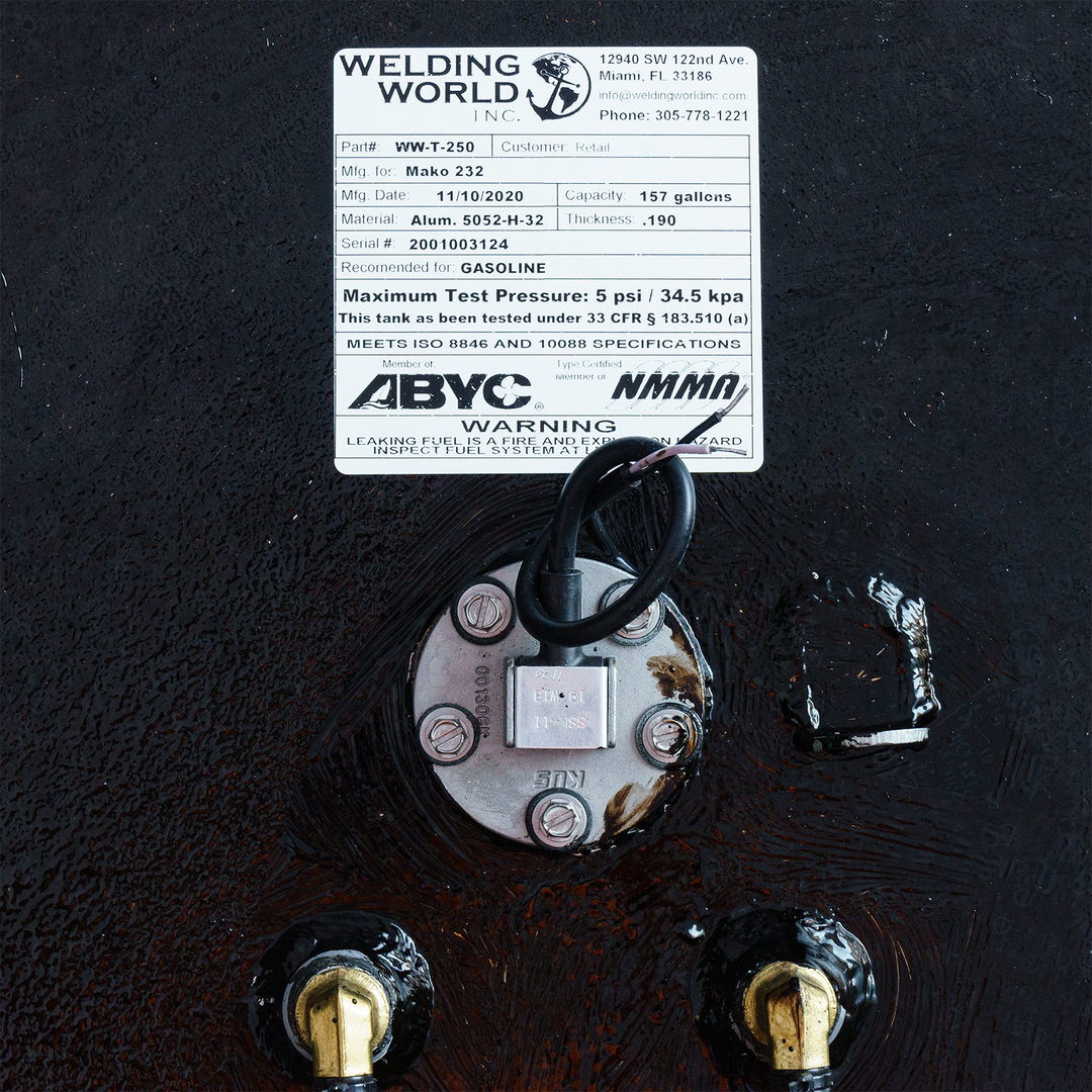 A close-up of a specification label from Welding World Inc., detailing the Mako 232 tank with part number WW-T-250. The label includes manufacturing date, capacity (157 gallons), material specifications, maximum test pressure, and safety warnings regarding leaking fuel hazards. It prominently features compliance certifications and a circular connection with wiring