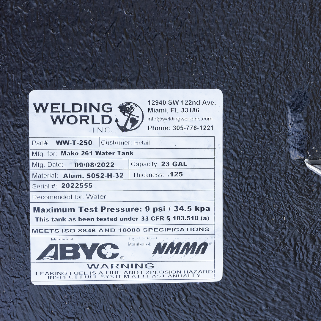 A close-up of a white manufacturer's label on a heavily textured black surface, with a white pipe visible along the right edge. The "Welding World, Inc." label identifies the product as a "Mako 261 Water Tank" with a 23-gallon capacity, made on September 8, 2022. Although recommended for water, the label includes a standard warning about fuel leaks and displays ABYC and NMMA compliance logos