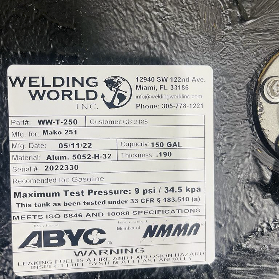 A white product label from "WELDING WORLD INC." is affixed to a black, textured surface. The label provides detailed specifications for a fuel tank: Part# WW-T-250, Mfg. for Mako 251, Mfg. Date 05/11/22, Capacity 150 GAL, Material Alum. 5052-H-32, Thickness .190, and Serial # 2022330. It is recommended for Gasoline, has a maximum test pressure of 9 psi / 34.5 kpa, and meets ISO 8846 and 10088 specifications. The label also includes contact information for Welding World Inc. and a warning about leaking fuel
