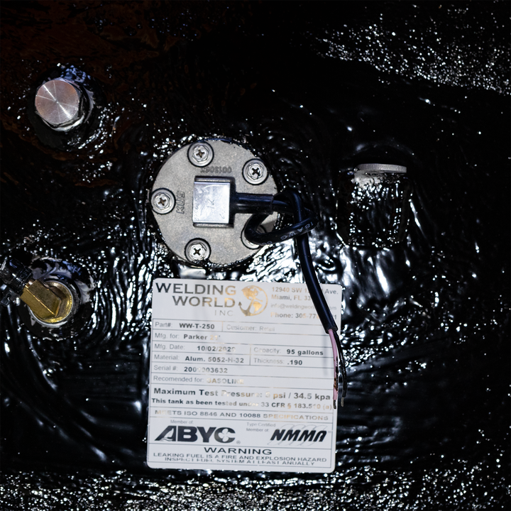 Close-up of a 1992 Parker 21' fuel tank featuring a 95-gallon capacity. The image shows the fuel tank's gauge and a label from Welding World, indicating the manufacturer's details, maximum test pressure of 34.5 kPa, and safety warnings. The tank is covered in a glossy black finish