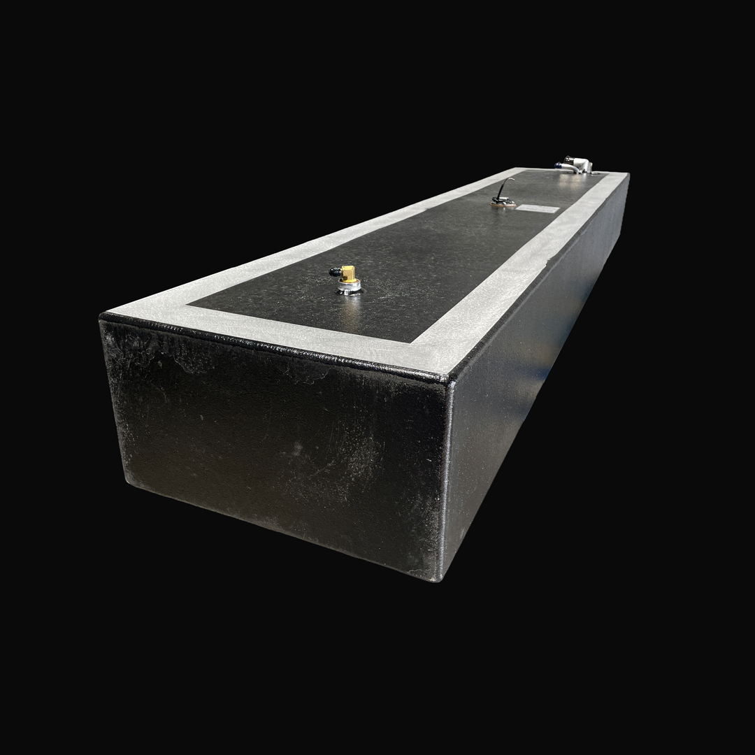 A studio high-angle isometric view showing the full length of a physical, finished black encapsulated Proline 21 OEM replacement marine fuel tank (84 gal 1994) from file image_1521da.jpg, isolated against a black background. Precision-fabricated from heavy-gauge marine-grade 5052-H32 aluminum, the long low-profile rectangular body is fully encapsulated in a protective, textured black TarGard epoxy coating with bare aluminum border margins framing the top deck. The top deck fitting layout features an aft-mou