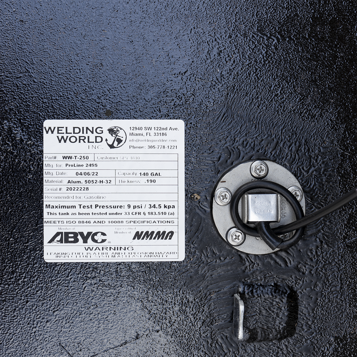 A white product label from "WELDING WORLD INC." is adhered to a textured black surface, likely a fuel tank. The label provides details for a ProLine 24SS fuel tank, Part# WW-T-250, manufactured on 04/06/22, with a capacity of 140 gallons, made of Alum. 5052-H-32, and a thickness of .190. The serial number is 2022228, and it's recommended for Gasoline with a maximum test pressure of 9 psi / 34.5 kpa. The label also states compliance with ISO 8846 and 10088 specifications and membership in ABYC and NMMA