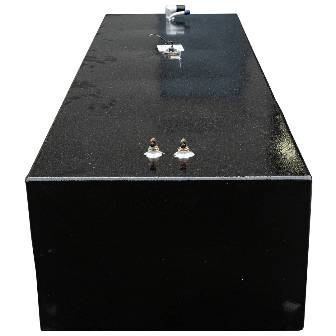 A top-down view of a rectangular, black fuel tank with a speckled, granular surface, set against a black and grey checkered background. The tank features various fittings, including two brass-colored valves with white bases, and a silver pipe with blue and black accents