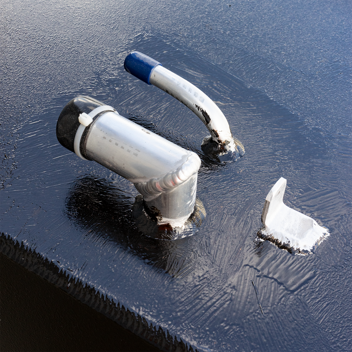 A close-up view of a black, textured surface, possibly a fuel tank, adorned with several metal components. These include two silver-colored pipes, one with a black cap and white zip tie, and the other with a blue cap, and a smaller, L-shaped silver bracket, all appearing to be welded or sealed to the surfac
