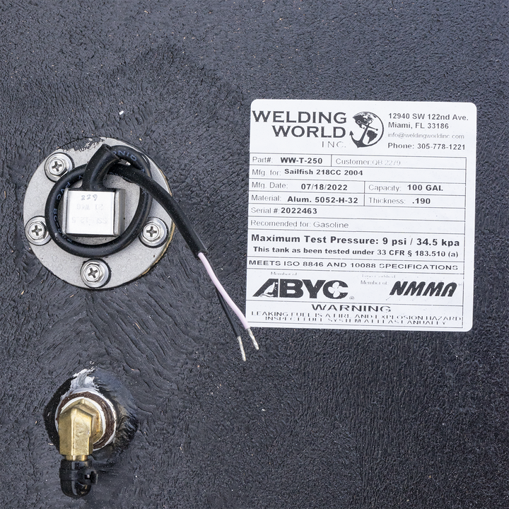 A white label from Welding World Inc. affixed to a black, textured surface. The label provides detailed information about a fuel tank, including Part# WW-T-250, Mfg. for Sailfish 218CC 2004, Mfg. Date 07/18/2022, Capacity 100 GAL, Material Alum. 5052-H-32, Thickness .190, and Serial # 2022463. It specifies the tank is recommended for gasoline, has a maximum test pressure of 9 psi / 34.5 kpa, and meets ISO 8846 and 10088 specifications. Below the label
