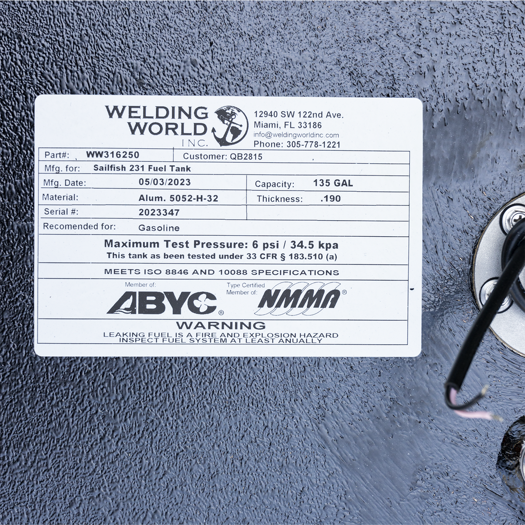 A white rectangular label affixed to a textured black surface, showing specifications for a Sailfish 231 Fuel Tank. The label includes the Welding World Inc. logo with an anchor graphic, contact information for the company in Miami, FL, and various details such as part number WW316250, customer QB2815, manufacturing date of 05/03/2023, material Aluminum 5052-H-32, thickness .190, serial number 2023347, and a capacity of 135 gallons. It also states the tank is recommended for gasoline