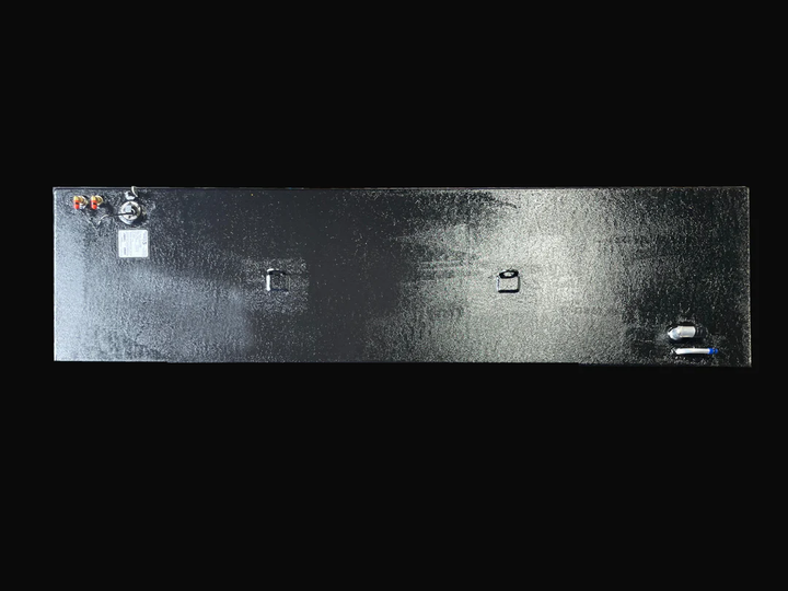 A direct top-down photo of a long, dark, textured boat fuel tank, showing its various top-mounted fittings, D-rings, and specification plate against a black background.