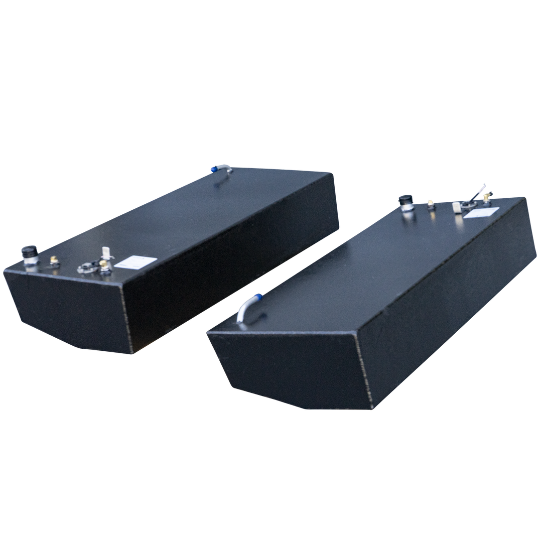 Two rectangular black fuel tanks, possibly made of aluminum, with various caps and nozzles on their top surfaces, are positioned against a black and grey checkered background
