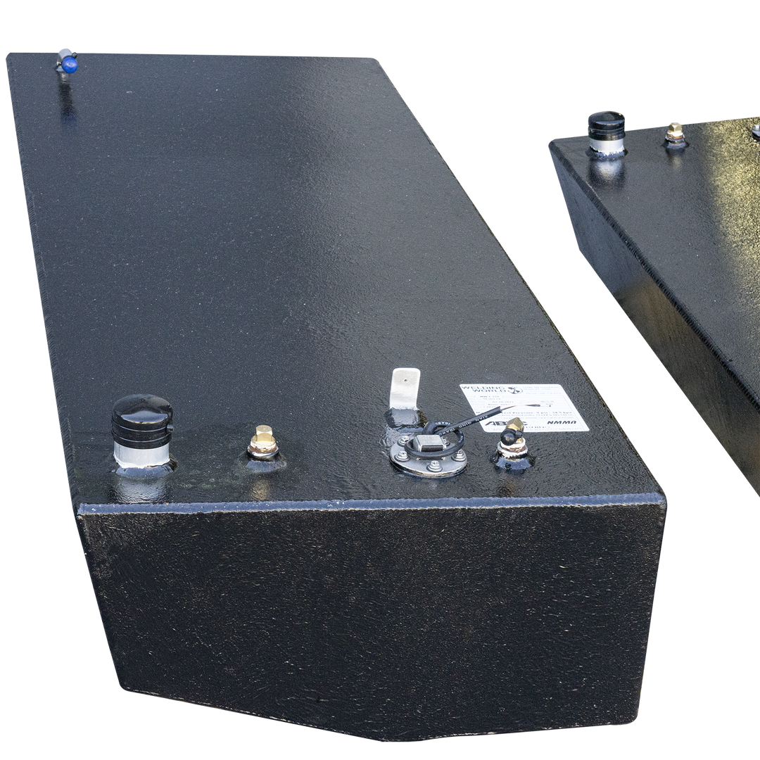 Two rectangular, dark grey fuel tanks, possibly made of aluminum, with various caps, nozzles, and a small white label on their top surfaces, are positioned against a black and grey checkered background