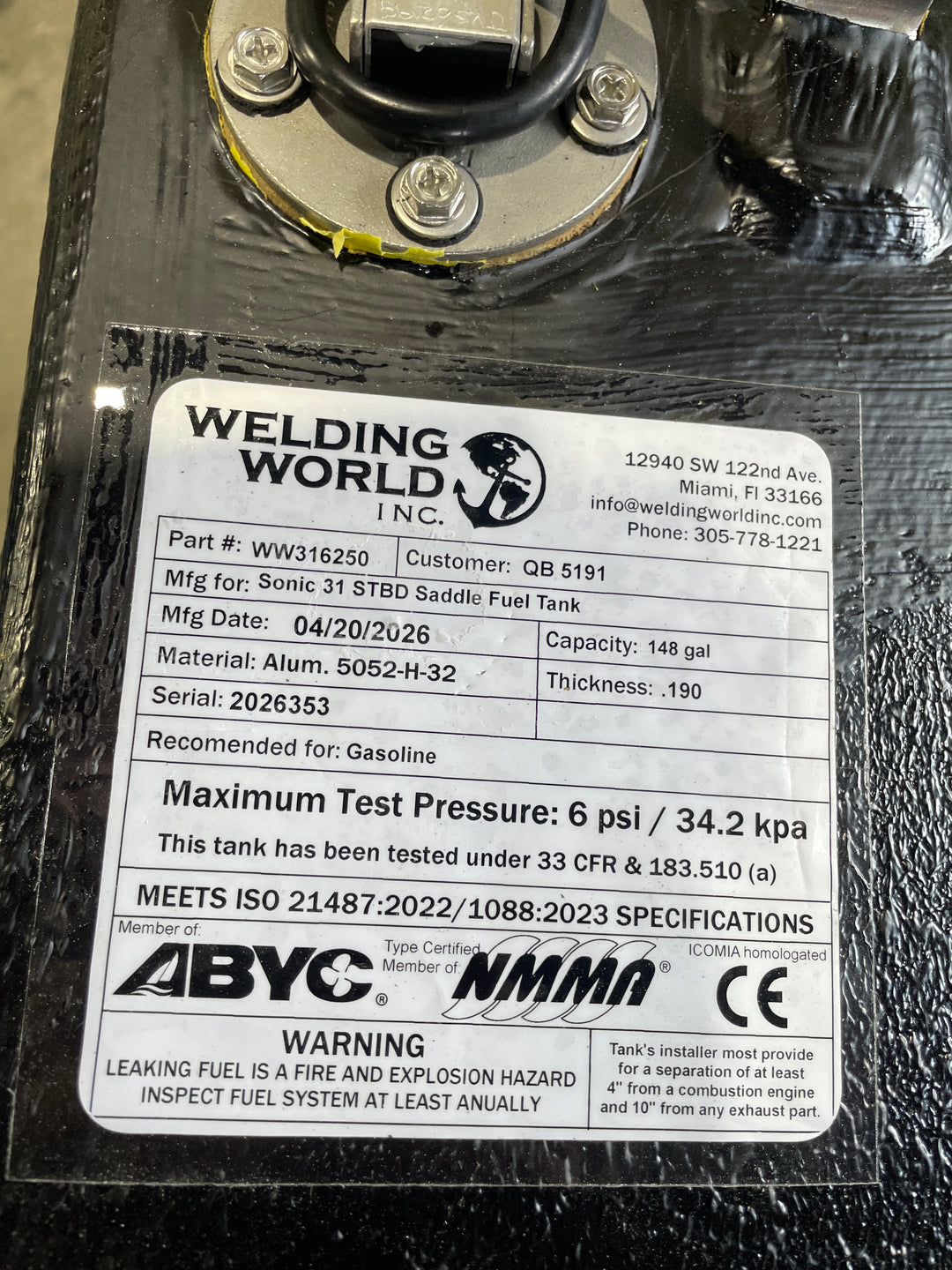Close-up of the Welding World Inc. manufacturing label for a Sonic 31 Starboard (STBD) Saddle fuel tank replacement. The certification tag confirms a 148-gallon capacity, heavy-duty .190" thickness 5052-H32 aluminum construction, and rigorous pressure testing at 6 psi. The label certifies full compliance with USCG 33 CFR § 183.510(a), ABYC, NMMA, and CE standards, ensuring a safe and legal OEM-quality replacement for marine gasoline systems.