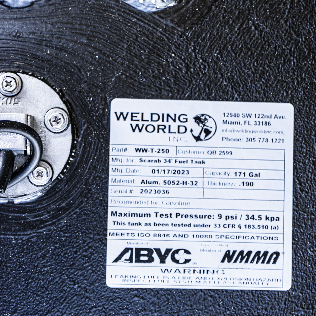 Close-up of a metal fuel tank surface showing a label from Welding World Inc. The label includes the company logo, address (12940 SW 122nd Ave, Miami, FL 33186), contact info, and tank specifications. The tank part number is WW-T-250, made for Scarab 34' Fuel Tank, manufactured on 01/17/2023. It has a capacity of 171 gallons, material is aluminum 5052-H-32, thickness .190 inches, and serial number 2023036. It is recommended for gasoline, has a maximum test pressure of 9 psi (34.5 kPa)