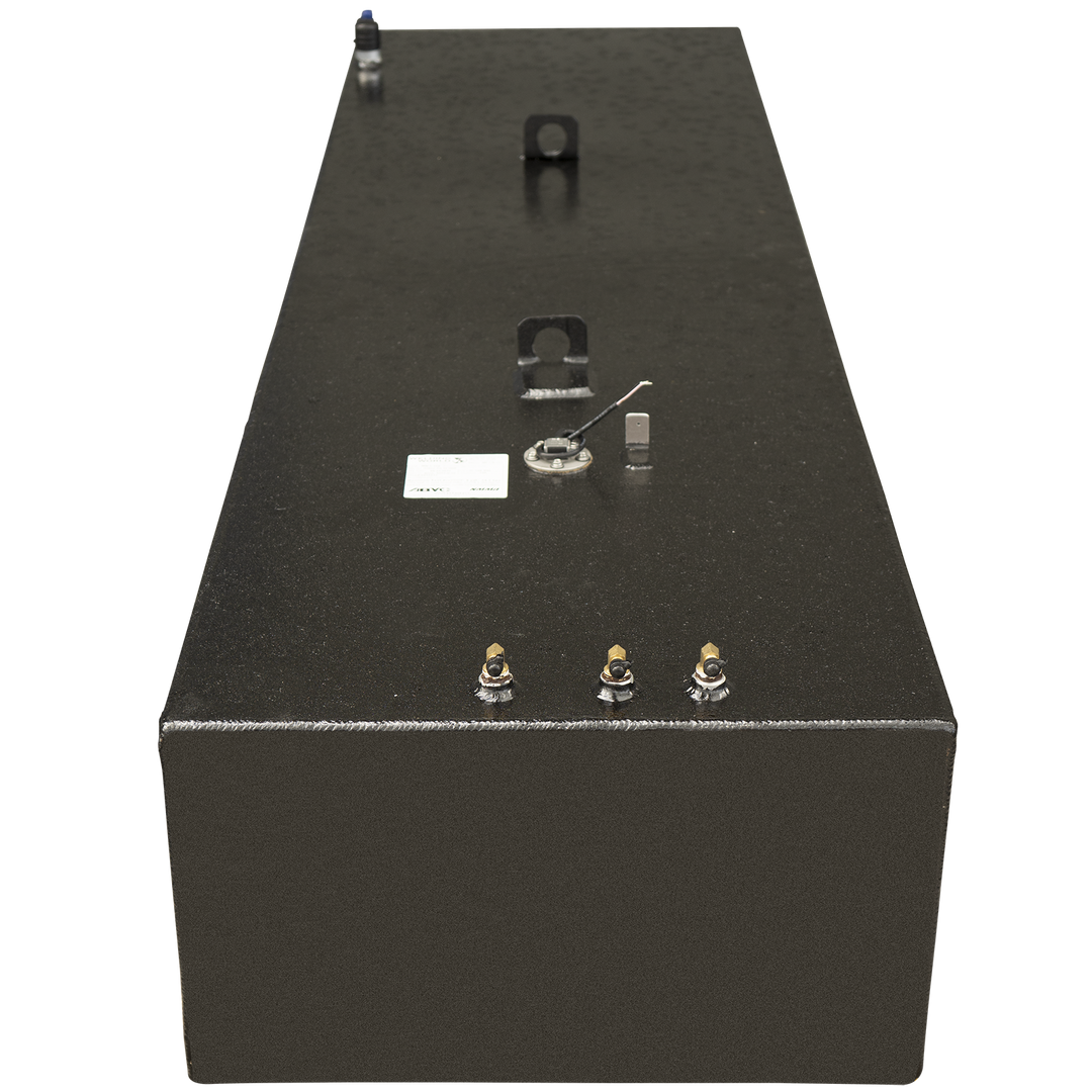 A long, black, rectangular fuel tank with a textured surface, shown from a slightly elevated, front-facing angle. The top of the tank features several components: three brass-colored fittings along the front edge, a small white label, a circular sensor with wires, a small rectangular component, and two curved metal mounting brackets. A blue-capped vent is visible at the far end of the tank